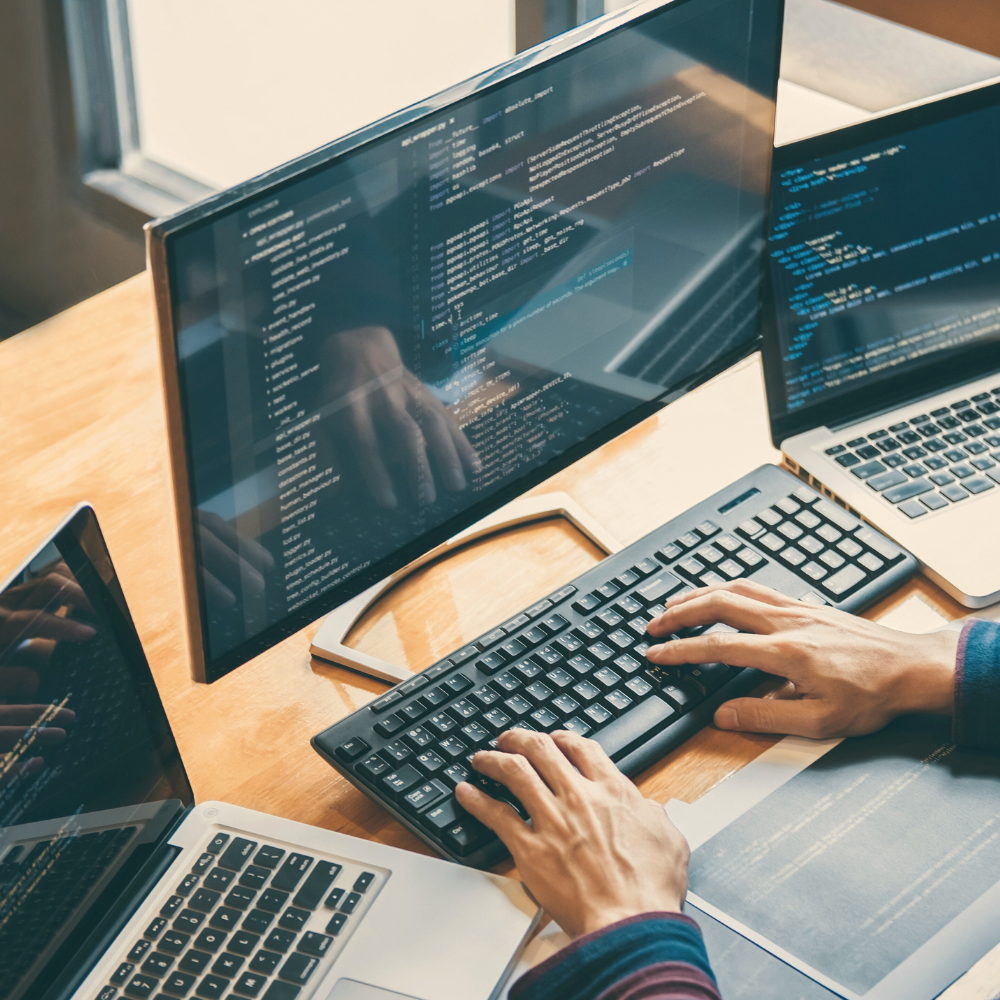 Ordentlich strukturierter Schreibtisch mit Laptop, Notizbuch, digitalen Tools und vielen Bildschirmen.