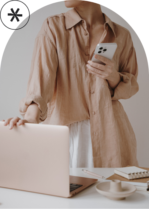 Erfolgreiche Unternehmerin mit Handy in der Hand, die andere Hand am Laptop.